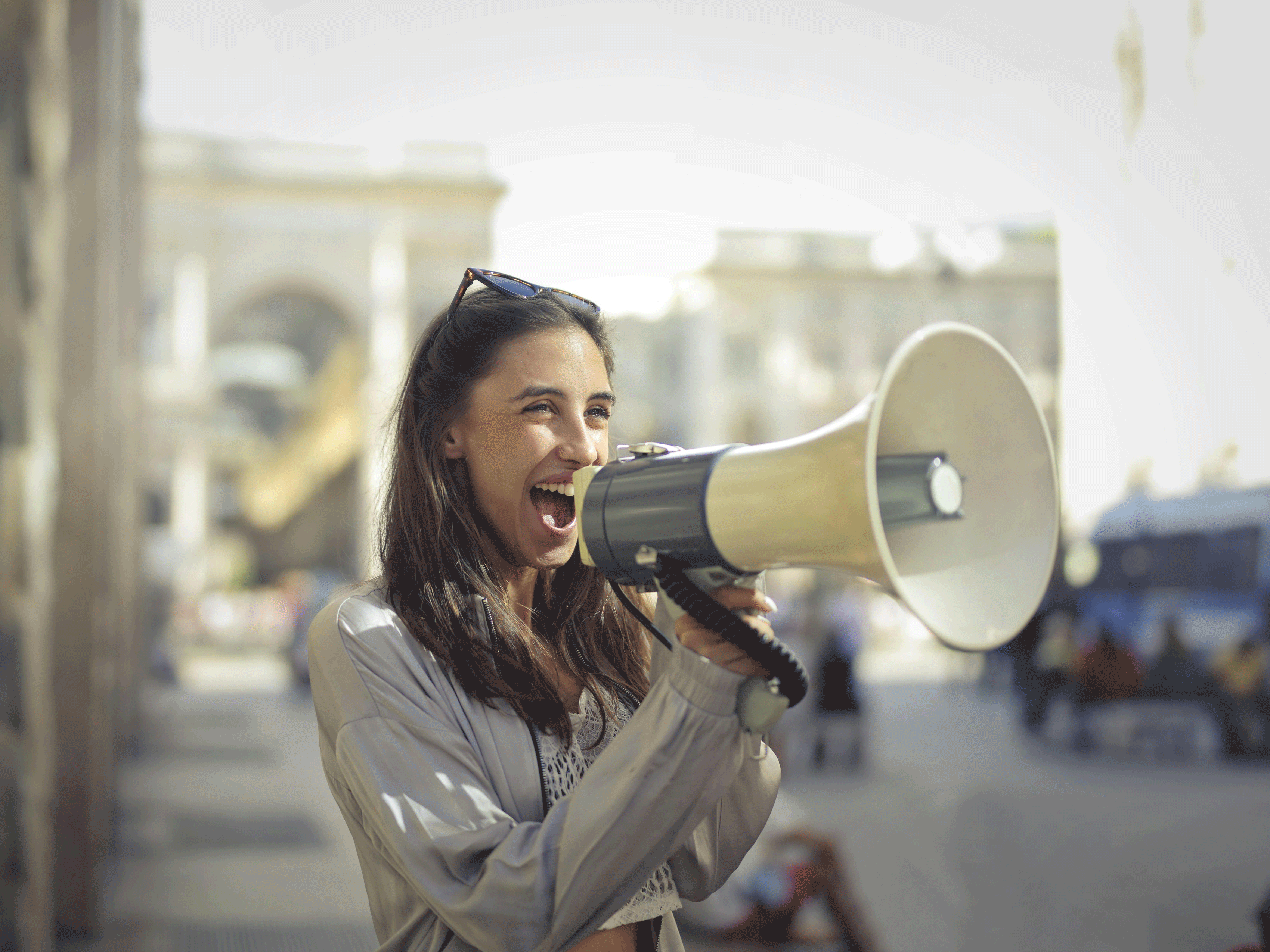 Frau steht mit Megaphone an einer Straße und ruft etwas.