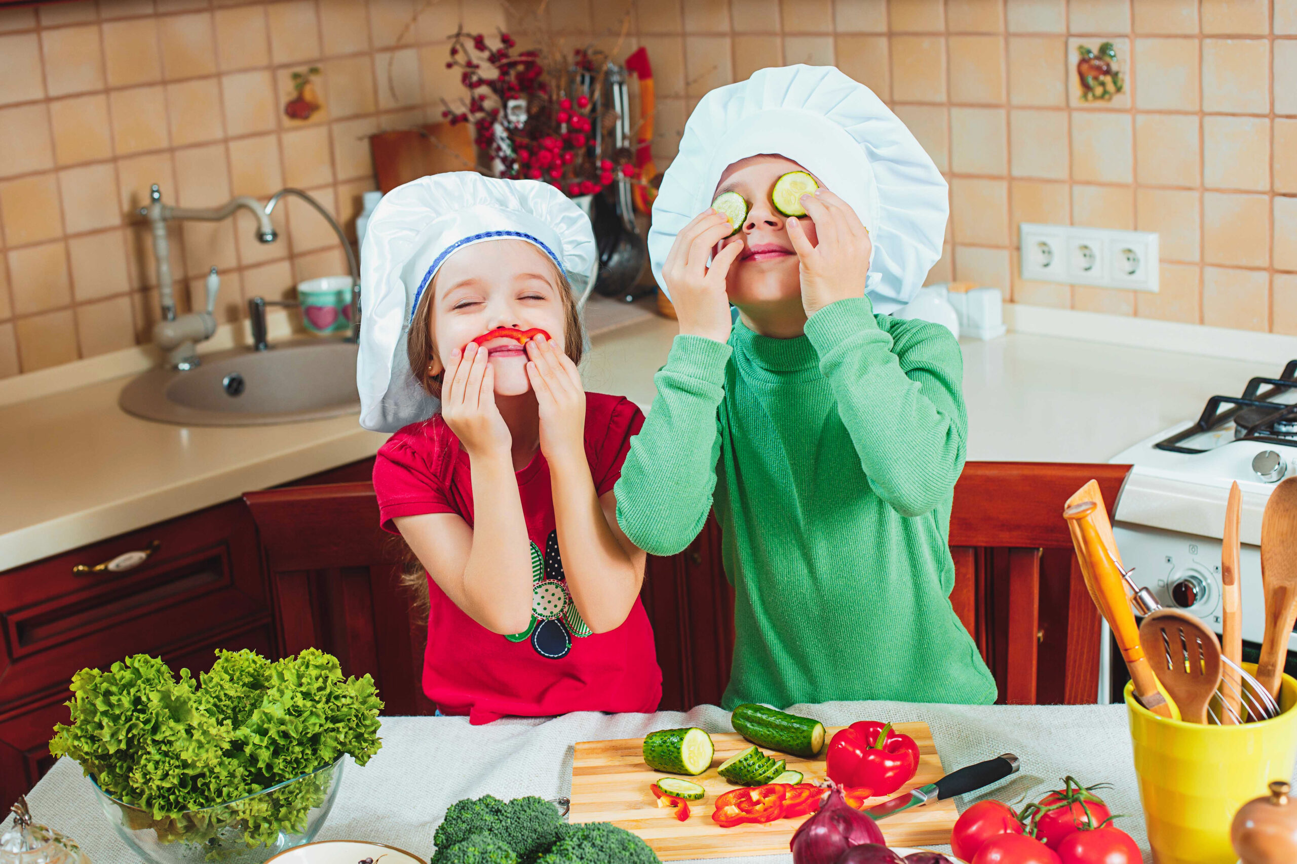 Lustige Kinder bereiten den frischen Gemüsesalat in der Küche vor