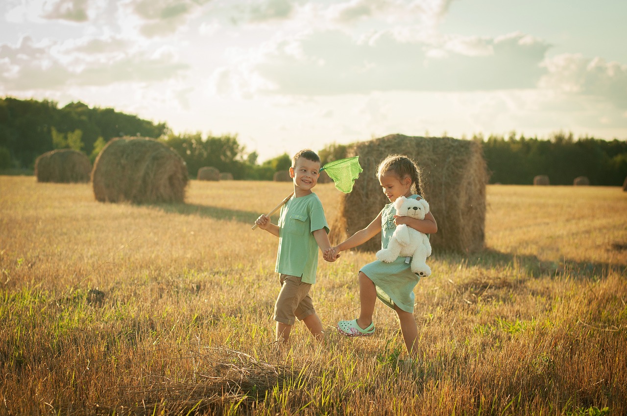 Zwei Kinder laufen Hand in Hand über ein gemähtes Feld.